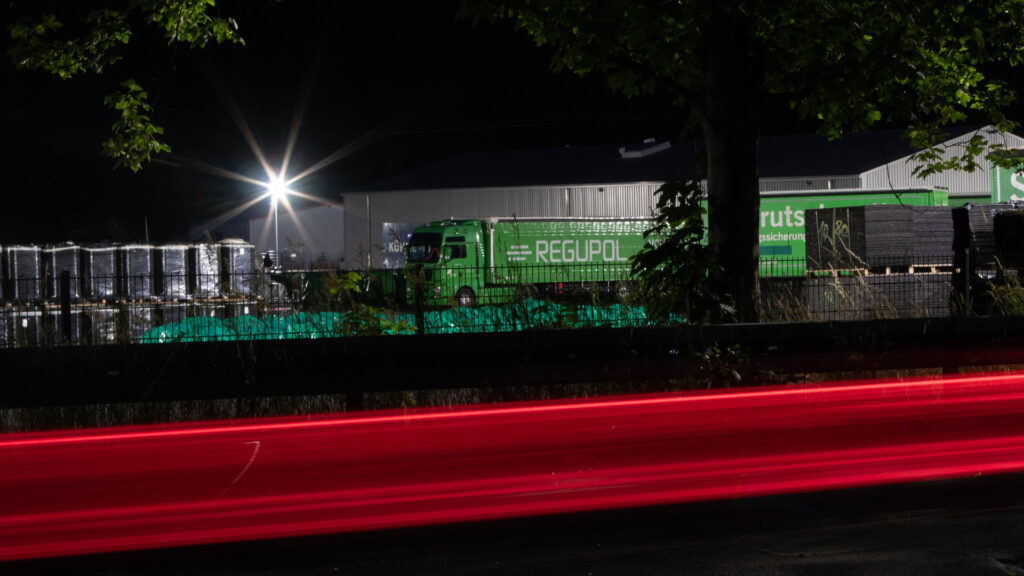LKW der Firma REGUPOL bei Nacht mit roten Lichtstreifen im Vordergrund